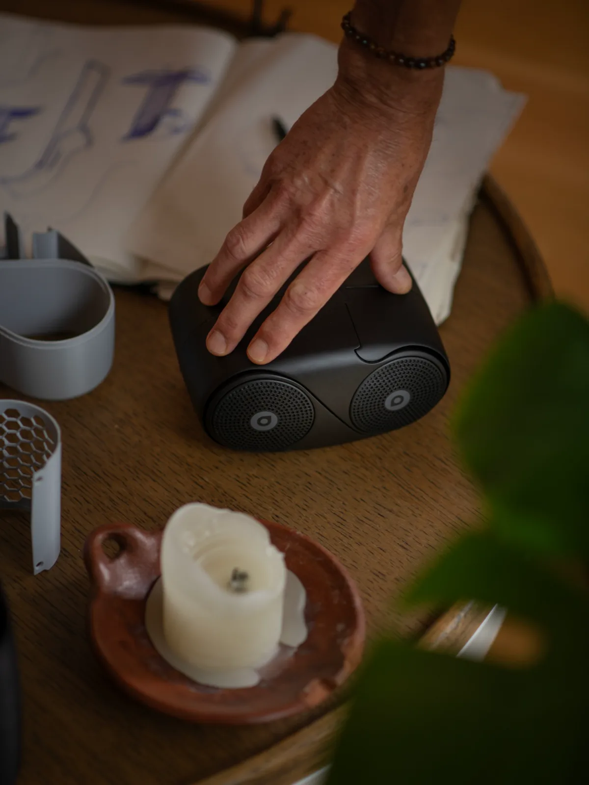 A hand resting on the closed CoAudio OneTwo beside design sketches and prototype parts